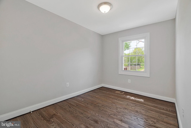empty room with dark wood-style flooring, baseboards, and visible vents