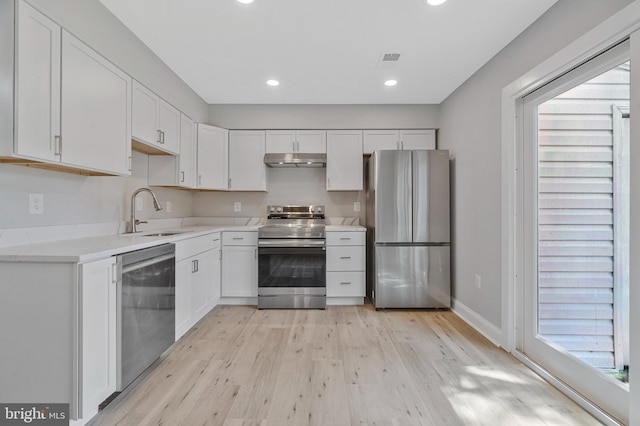 kitchen with white cabinets, a sink, light wood-style floors, stainless steel appliances, and under cabinet range hood