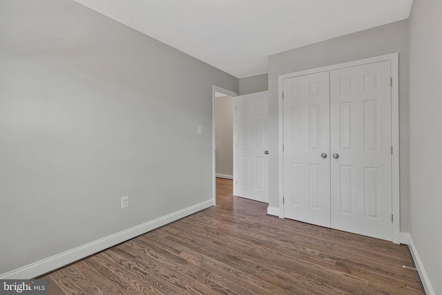 unfurnished bedroom featuring baseboards, wood finished floors, and a closet