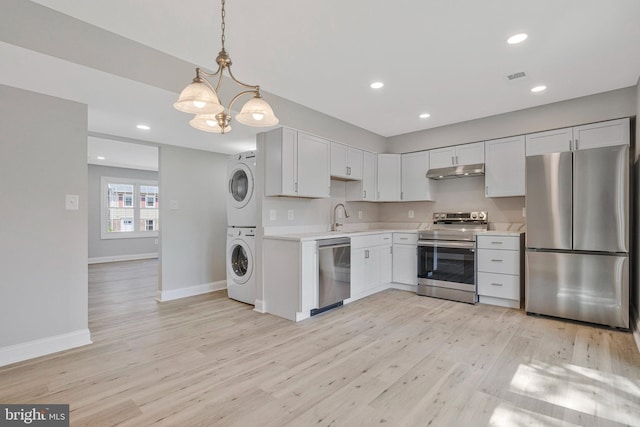 kitchen featuring stacked washer and dryer, baseboards, light countertops, under cabinet range hood, and stainless steel appliances