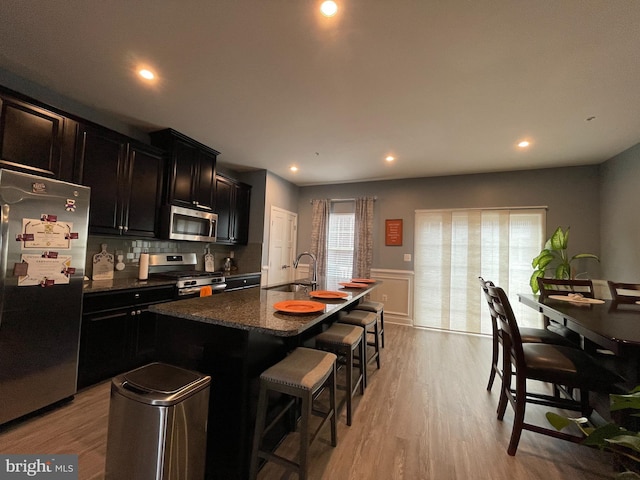 14503 Hunts Farm Rd, Brandywine, MD 20613 - kitchen with stainless steel appliances, a breakfast bar, a center island with sink, dark cabinetry, and light wood-style floors