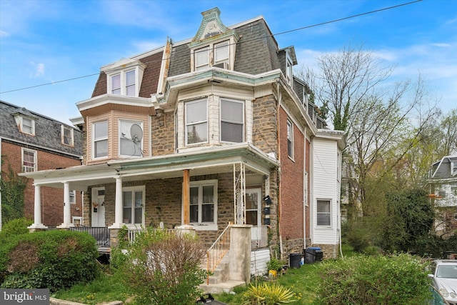 second empire-style home with a porch, mansard roof, and stone siding