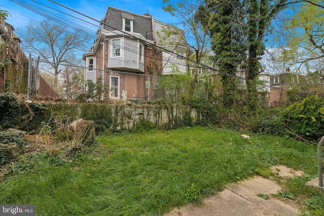 exterior space with fence, mansard roof, and brick siding