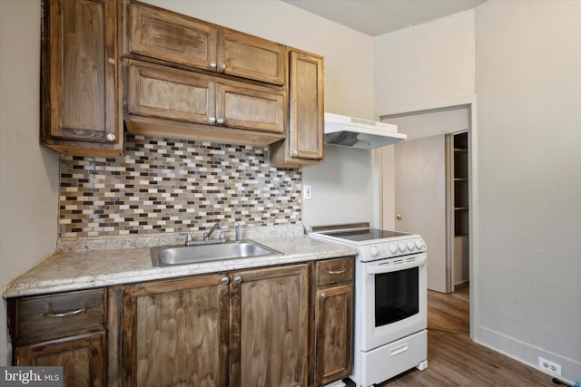 kitchen featuring white electric range oven, light countertops, under cabinet range hood, a sink, and backsplash