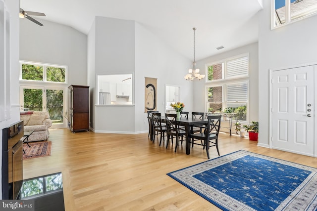 dining space featuring high vaulted ceiling, a chandelier, wood finished floors, ceiling fan, and baseboards