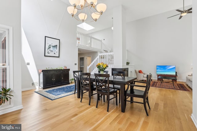 dining area featuring high vaulted ceiling, stairs, light wood-type flooring, a chandelier, and ceiling fan