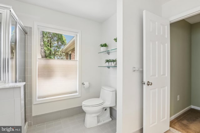 full bath featuring toilet, a tile shower, and baseboards