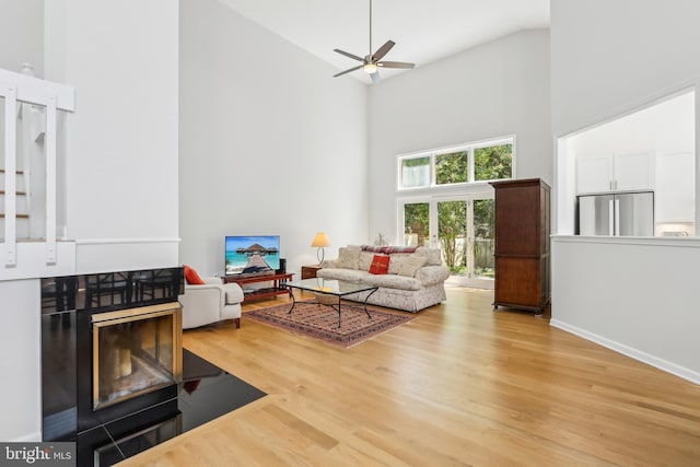 living area featuring high vaulted ceiling, light wood-style flooring, a ceiling fan, and baseboards