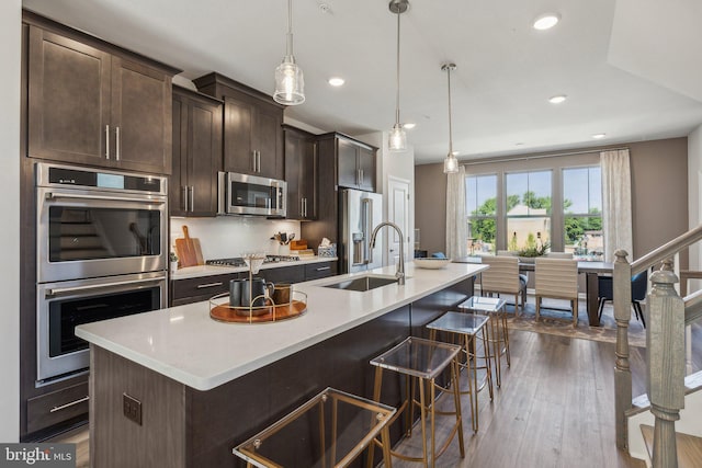 kitchen with dark brown cabinets, a sink, light countertops, an island with sink, and stainless steel appliances