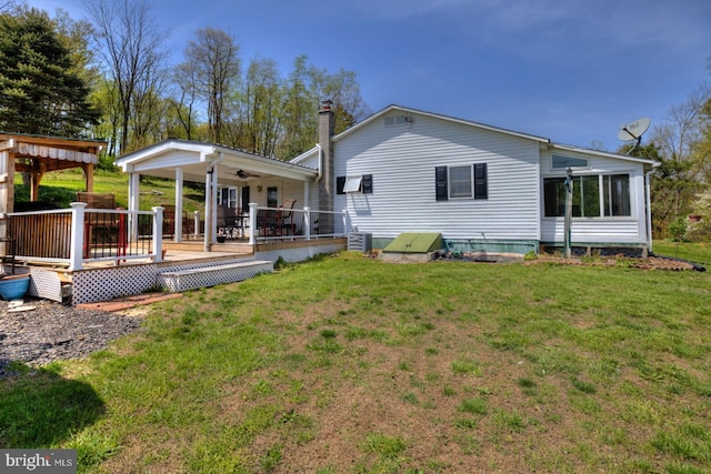 rear view of house featuring a chimney, a yard, a deck, and ceiling fan