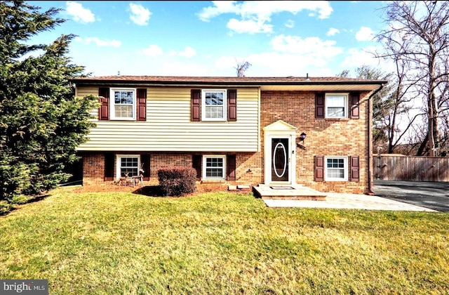 raised ranch featuring brick siding, fence, and a front yard