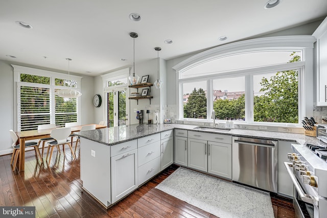 kitchen featuring stainless steel appliances, a sink, a peninsula, dark wood-style floors, and light stone counters
