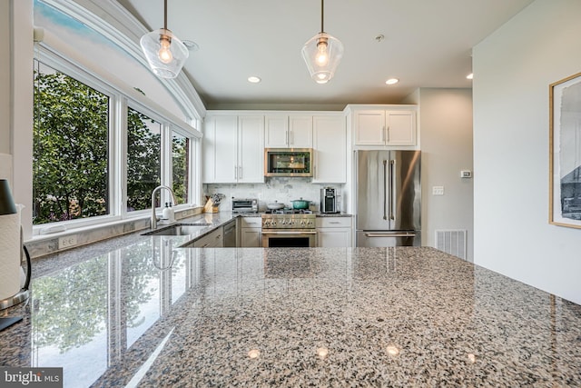 kitchen featuring high end appliances, a sink, decorative backsplash, stone counters, and white cabinetry