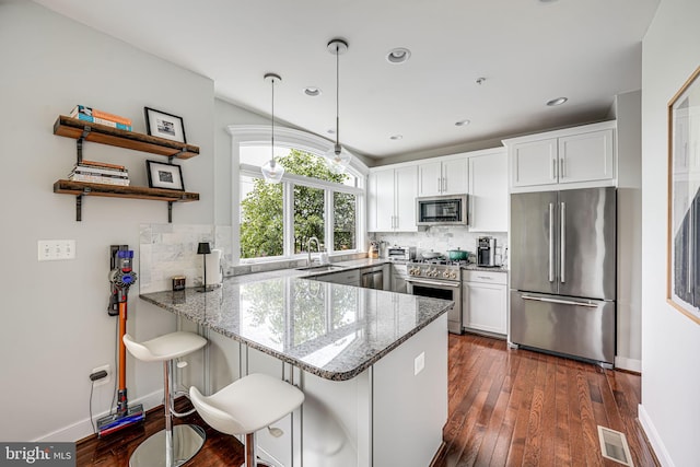kitchen with appliances with stainless steel finishes, a sink, a peninsula, dark wood-style floors, and white cabinets