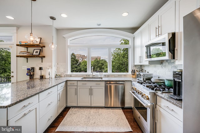 kitchen featuring appliances with stainless steel finishes, a sink, tasteful backsplash, white cabinetry, and a peninsula