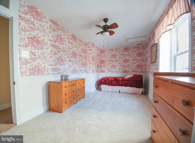 carpeted bedroom featuring wallpapered walls, wainscoting, and ceiling fan