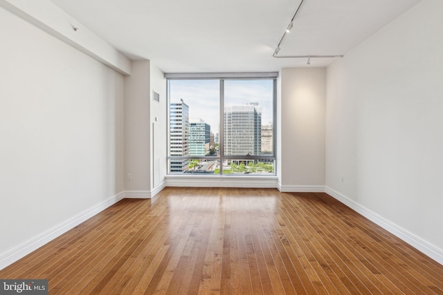 spare room featuring track lighting, baseboards, wood finished floors, visible vents, and a city view