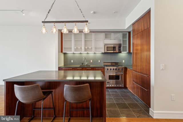 kitchen with decorative backsplash, dark countertops, a breakfast bar area, a sink, and stainless steel appliances