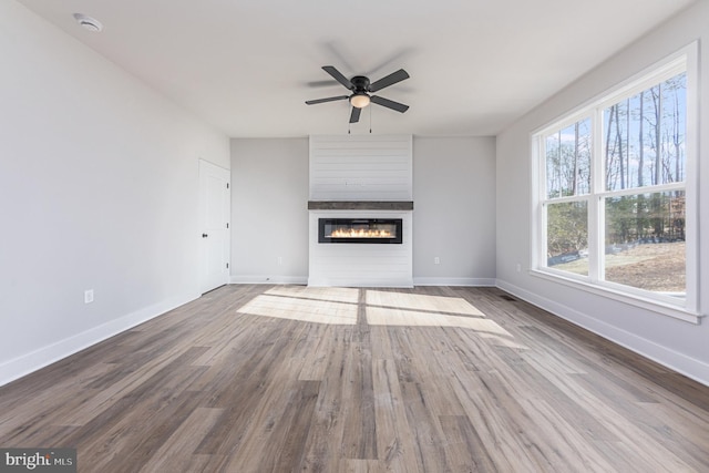 unfurnished living room with baseboards, ceiling fan, wood finished floors, and a fireplace