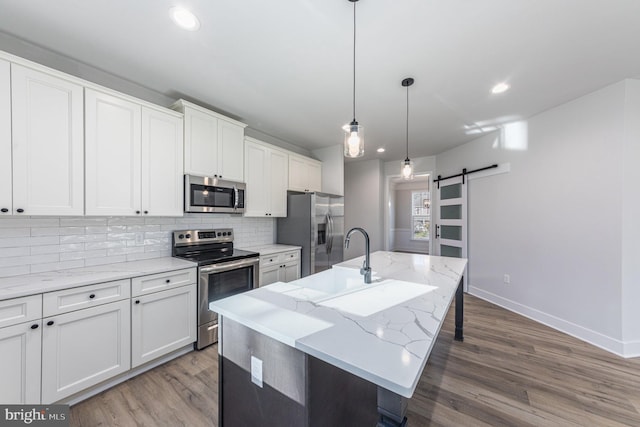 kitchen with wood finished floors, an island with sink, a barn door, tasteful backsplash, and appliances with stainless steel finishes