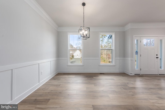 unfurnished dining area featuring an inviting chandelier, ornamental molding, wainscoting, and wood finished floors