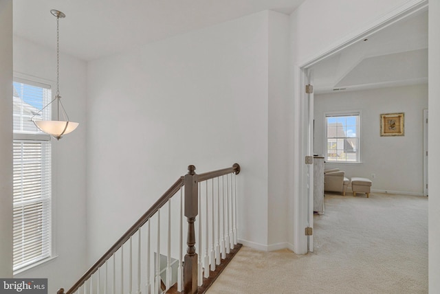 hallway with carpet floors, baseboards, and an upstairs landing