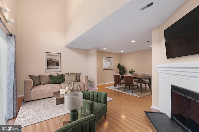 living room featuring wood finished floors, baseboards, a brick fireplace, and recessed lighting