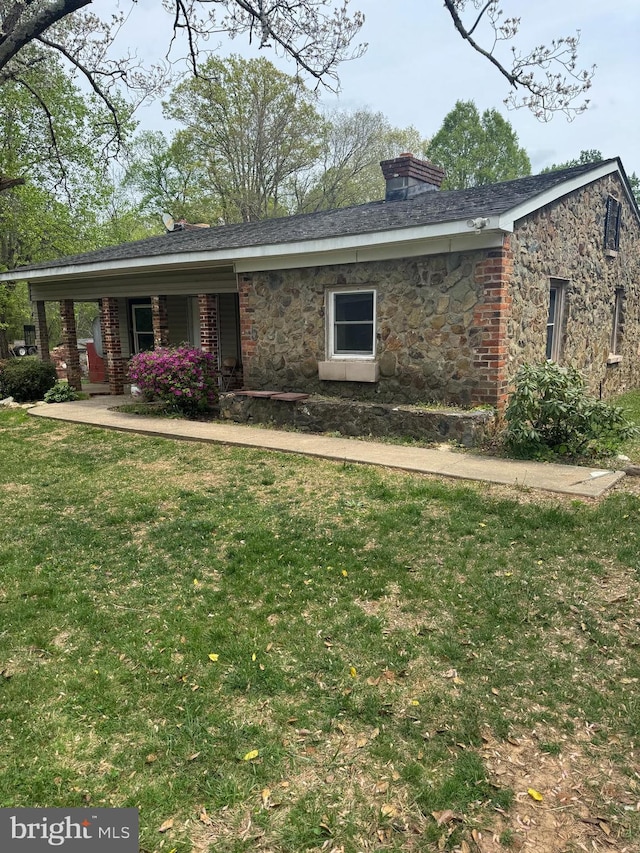 view of front of property featuring a chimney, a front lawn, covered porch, and stone siding