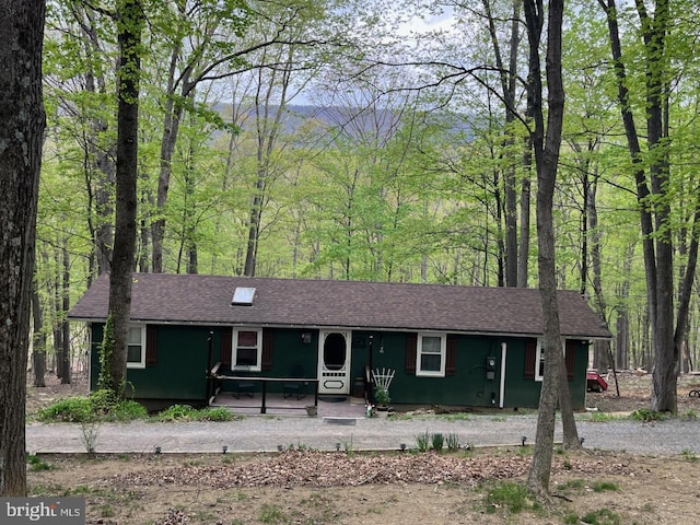 ranch-style home featuring roof with shingles, covered porch, and a wooded view