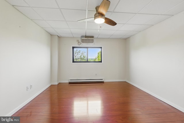 empty room with ceiling fan, baseboard heating, baseboards, a drop ceiling, and wood finished floors
