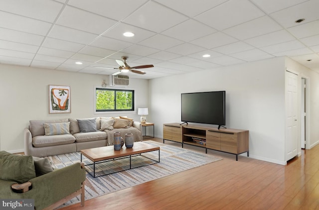 living area featuring ceiling fan, a paneled ceiling, a wall mounted AC, wood finished floors, and baseboards