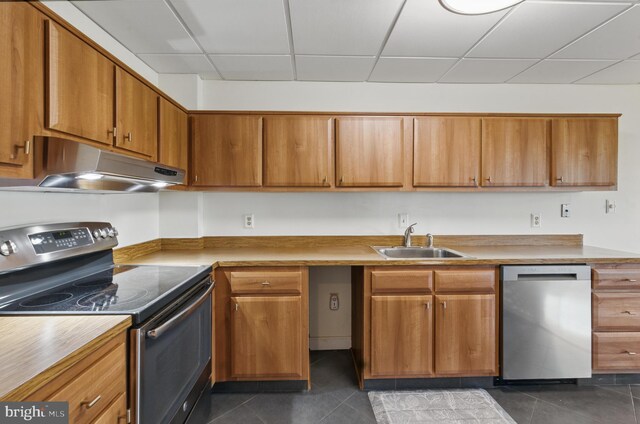 kitchen with a sink, dark tile patterned flooring, stainless steel appliances, and under cabinet range hood