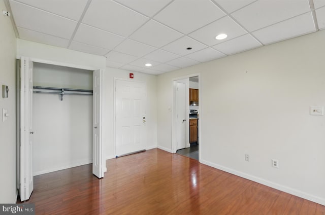 unfurnished bedroom featuring baseboards, a drop ceiling, a closet, and dark wood finished floors
