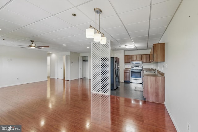 unfurnished living room with ceiling fan, a sink, baseboards, dark wood-style floors, and a drop ceiling