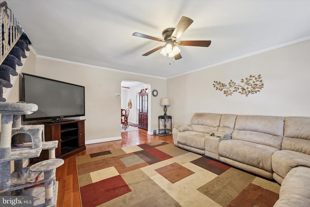 living room featuring crown molding, wood finished floors, baseboards, ceiling fan, and arched walkways