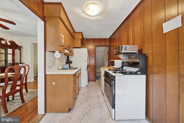 kitchen featuring wood walls, white appliances, light countertops, brown cabinets, and a ceiling fan