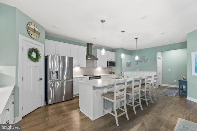 kitchen featuring a sink, wall chimney exhaust hood, dark wood-type flooring, stainless steel appliances, and a kitchen island with sink