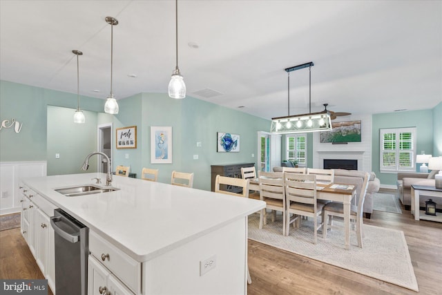 kitchen with a sink, white cabinetry, open floor plan, stainless steel dishwasher, and light wood-style floors