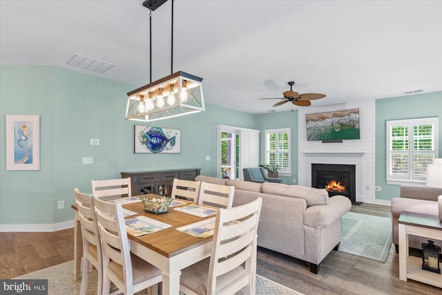 dining room with a fireplace, ceiling fan, visible vents, and wood finished floors