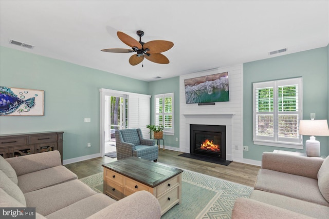 living room featuring a fireplace, ceiling fan, visible vents, and wood finished floors