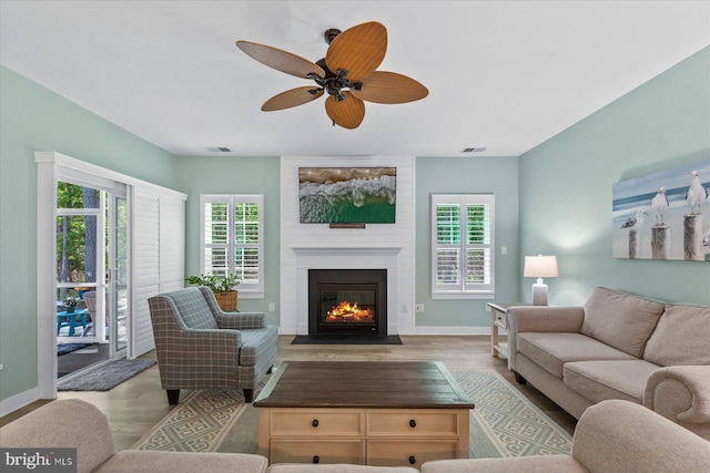 living room with a brick fireplace, a wealth of natural light, ceiling fan, and wood finished floors
