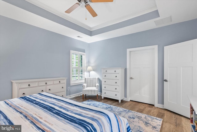bedroom featuring baseboards, a raised ceiling, visible vents, and wood finished floors