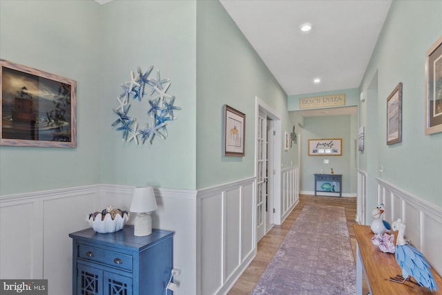 corridor with french doors, a wainscoted wall, light wood-type flooring, a decorative wall, and recessed lighting