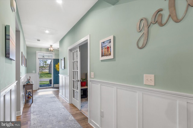 hallway with a decorative wall, french doors, wood finished floors, recessed lighting, and wainscoting