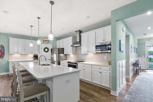 kitchen featuring a sink, stainless steel appliances, wall chimney exhaust hood, dark wood-style flooring, and a kitchen bar