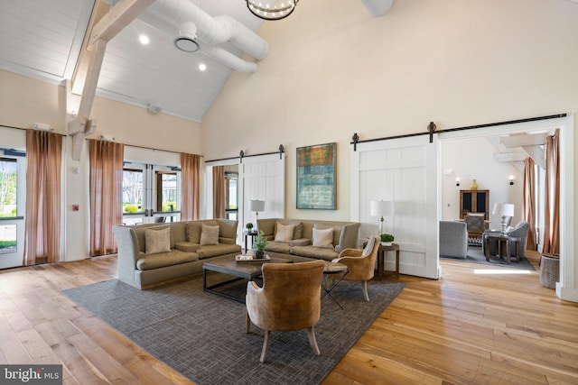 living area featuring high vaulted ceiling, a barn door, beam ceiling, and light wood finished floors