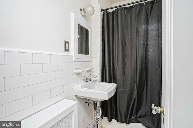 bathroom featuring a shower with curtain, tile walls, a sink, and a wainscoted wall