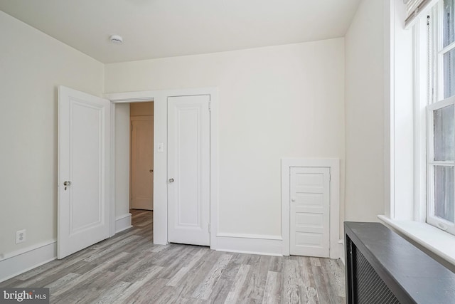 unfurnished bedroom featuring baseboards, light wood finished floors, and multiple windows