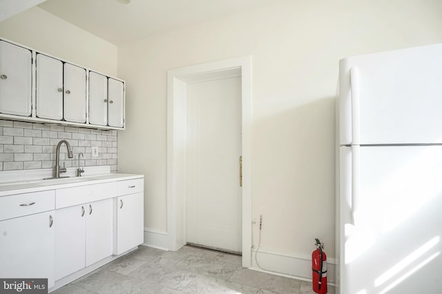 kitchen featuring freestanding refrigerator, decorative backsplash, light countertops, white cabinets, and a sink