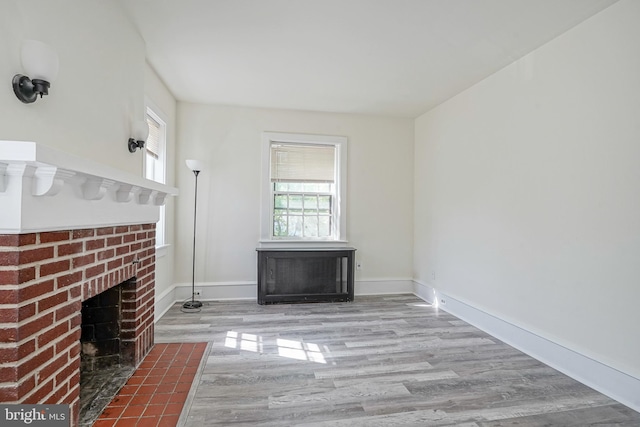 unfurnished living room featuring baseboards, a brick fireplace, and wood finished floors